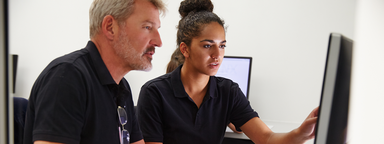 a young woman helping an older man with work at a computer