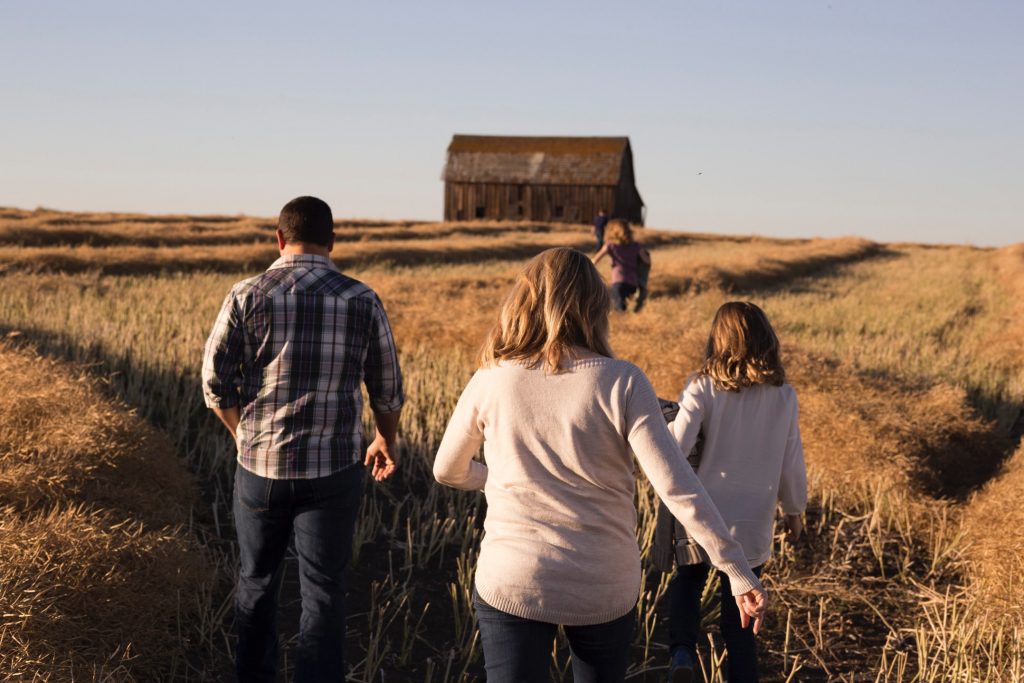 Man, woman and three children walking in a field toward a barn.