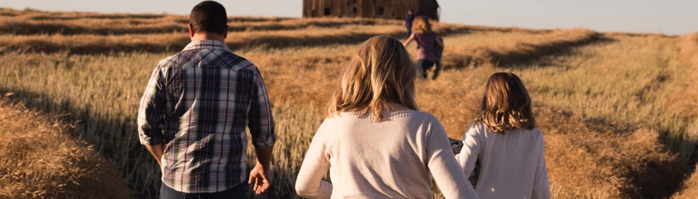 Man, woman and three children walking in a field toward a barn.