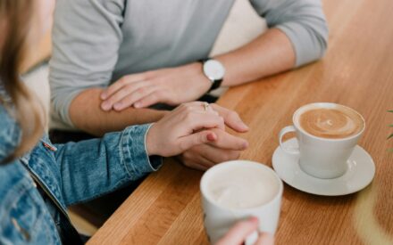 A couple holding hands next to two cups of coffee