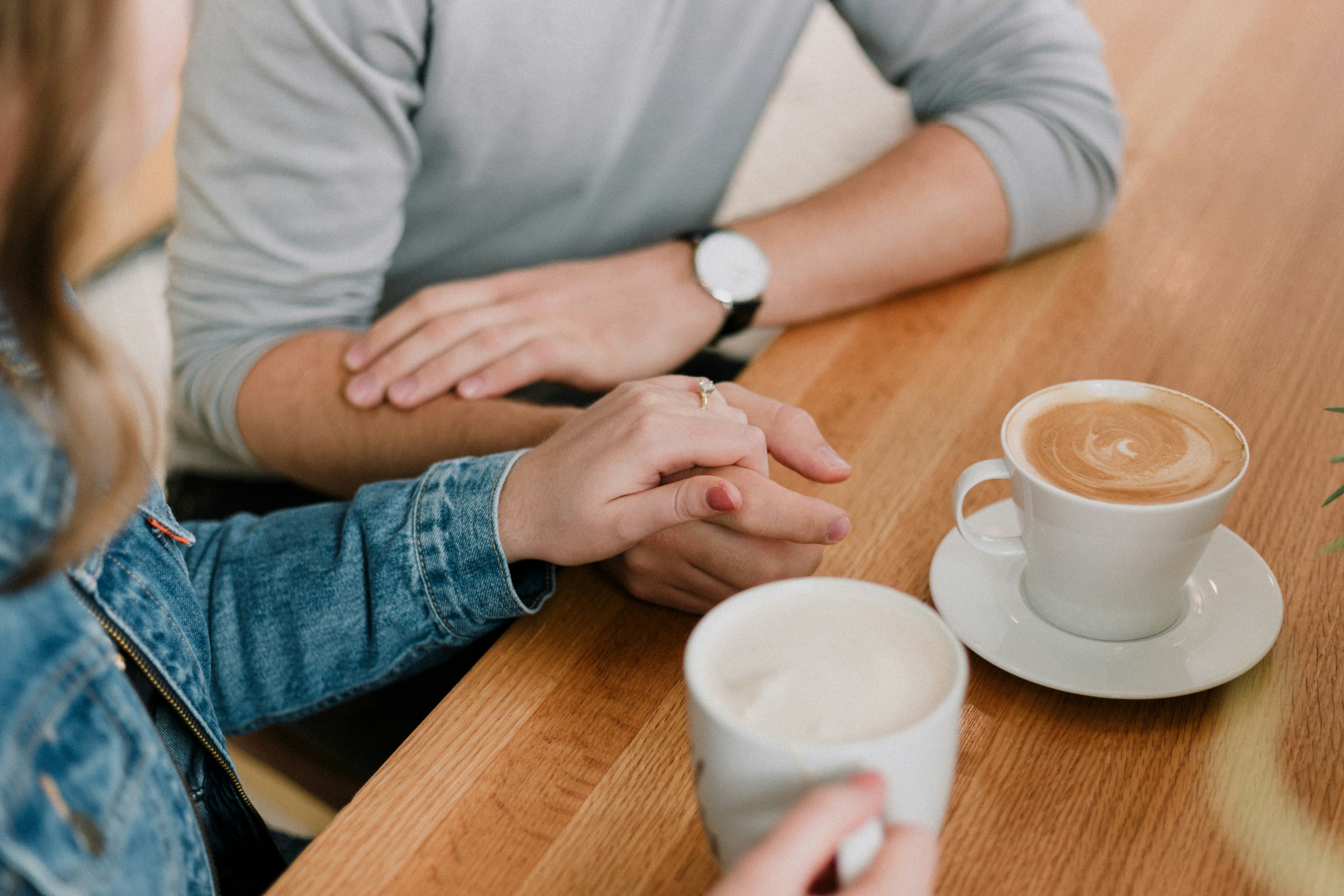 A couple holding hands next to two cups of coffee